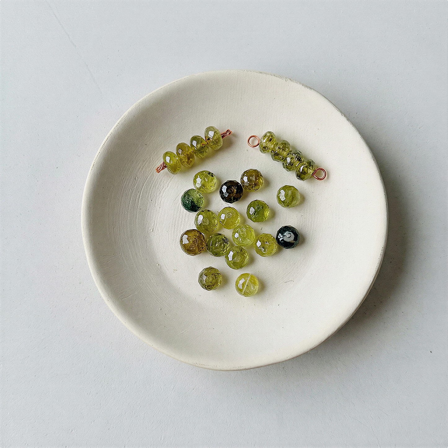 Faceted green garnet rondelle bead resting on natural stone surface in soft, diffused daylight