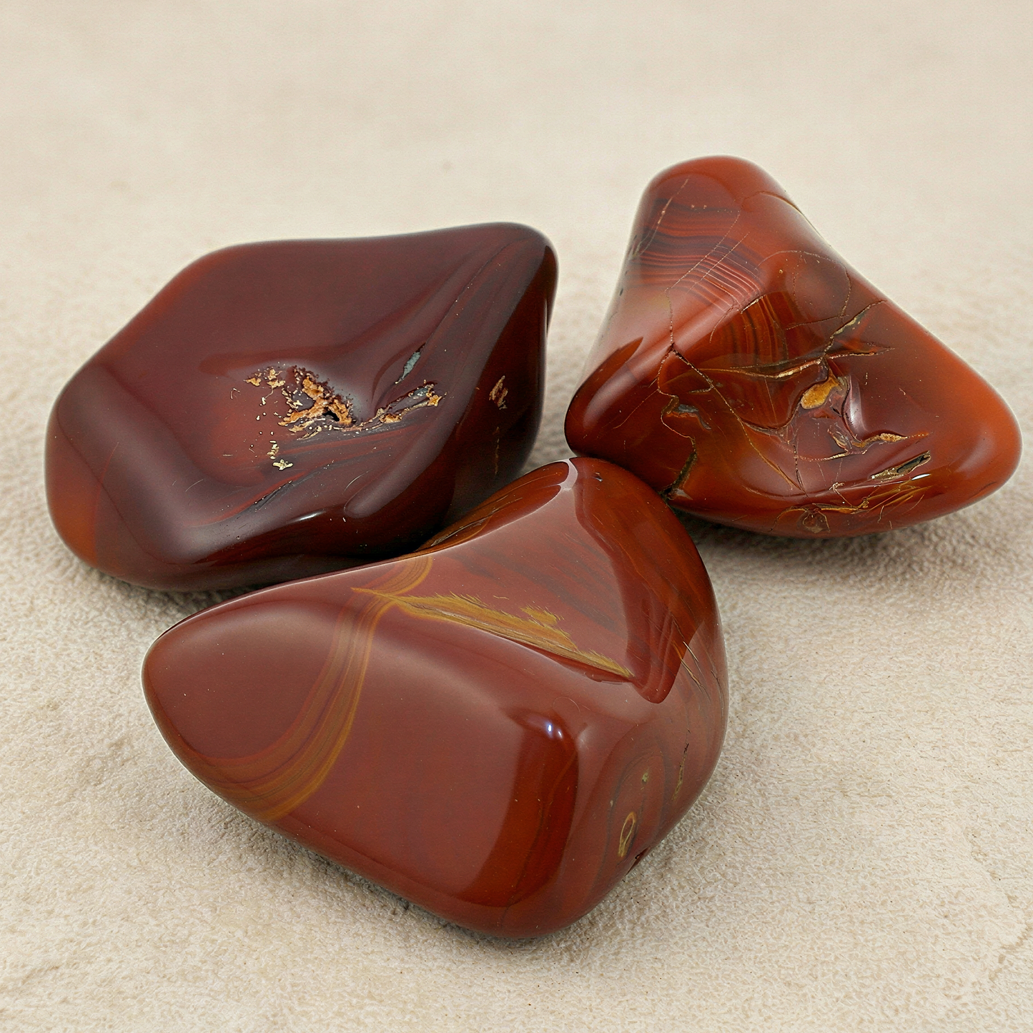 Dark red carnelian tumbled stone on neutral stone surface with refined lighting enhancing natural clarity and depth