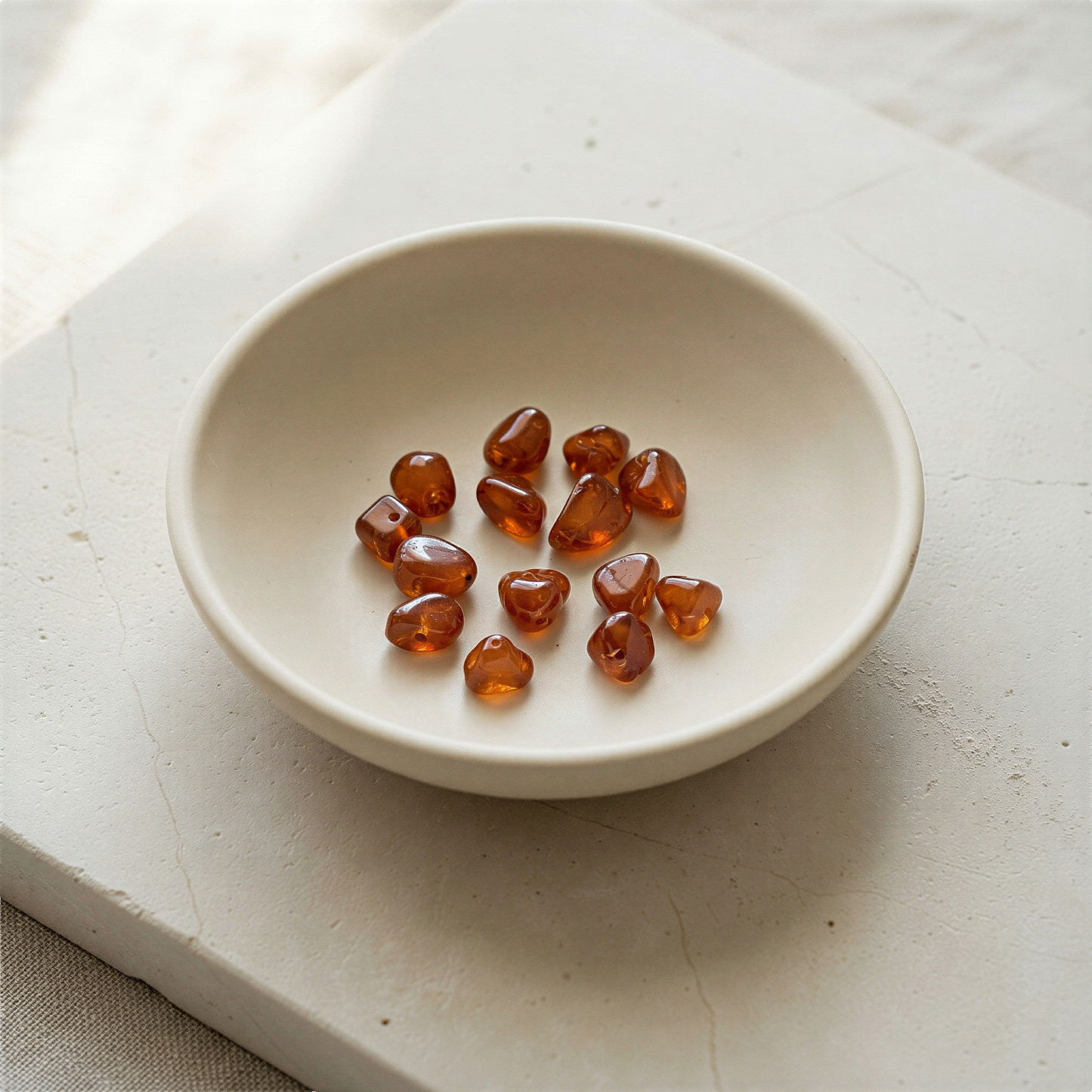 Tiny spessartite garnet tumbled nugget bead resting on natural stone surface in soft, ambient daylight