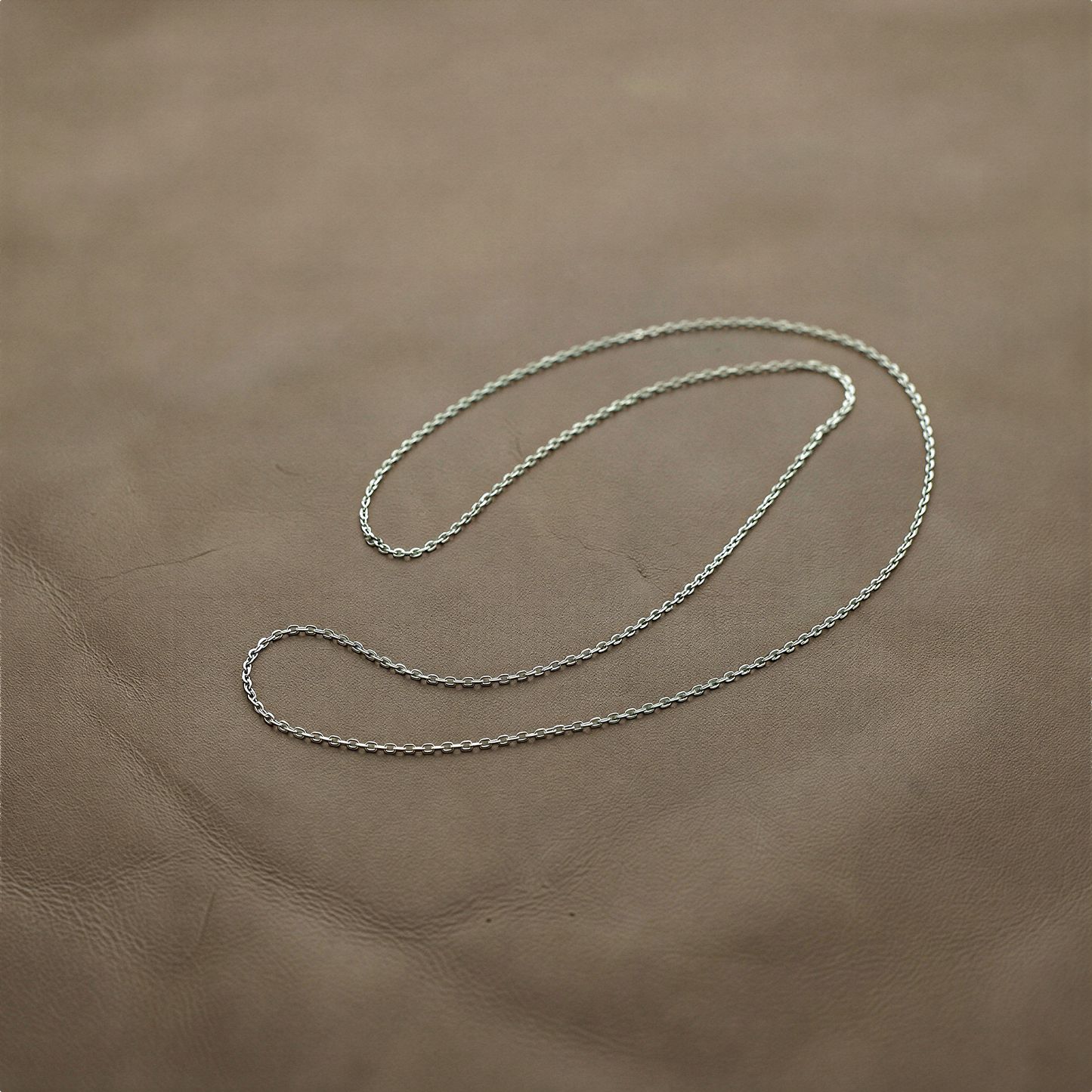 Sterling silver flat cable chain resting on jade stone with soft diffused light and natural textures