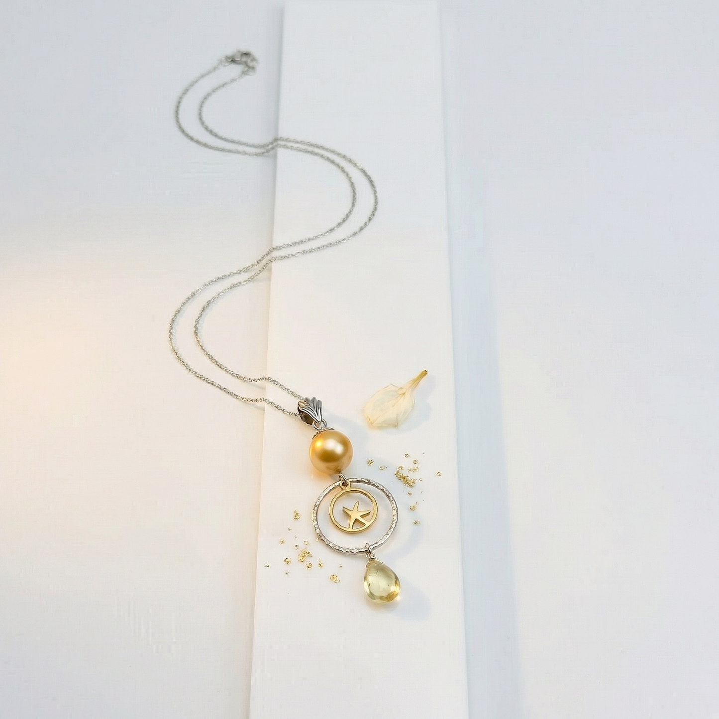 Golden pearl pendant on white acrylic with jasmine petal and pale gold leaf dust