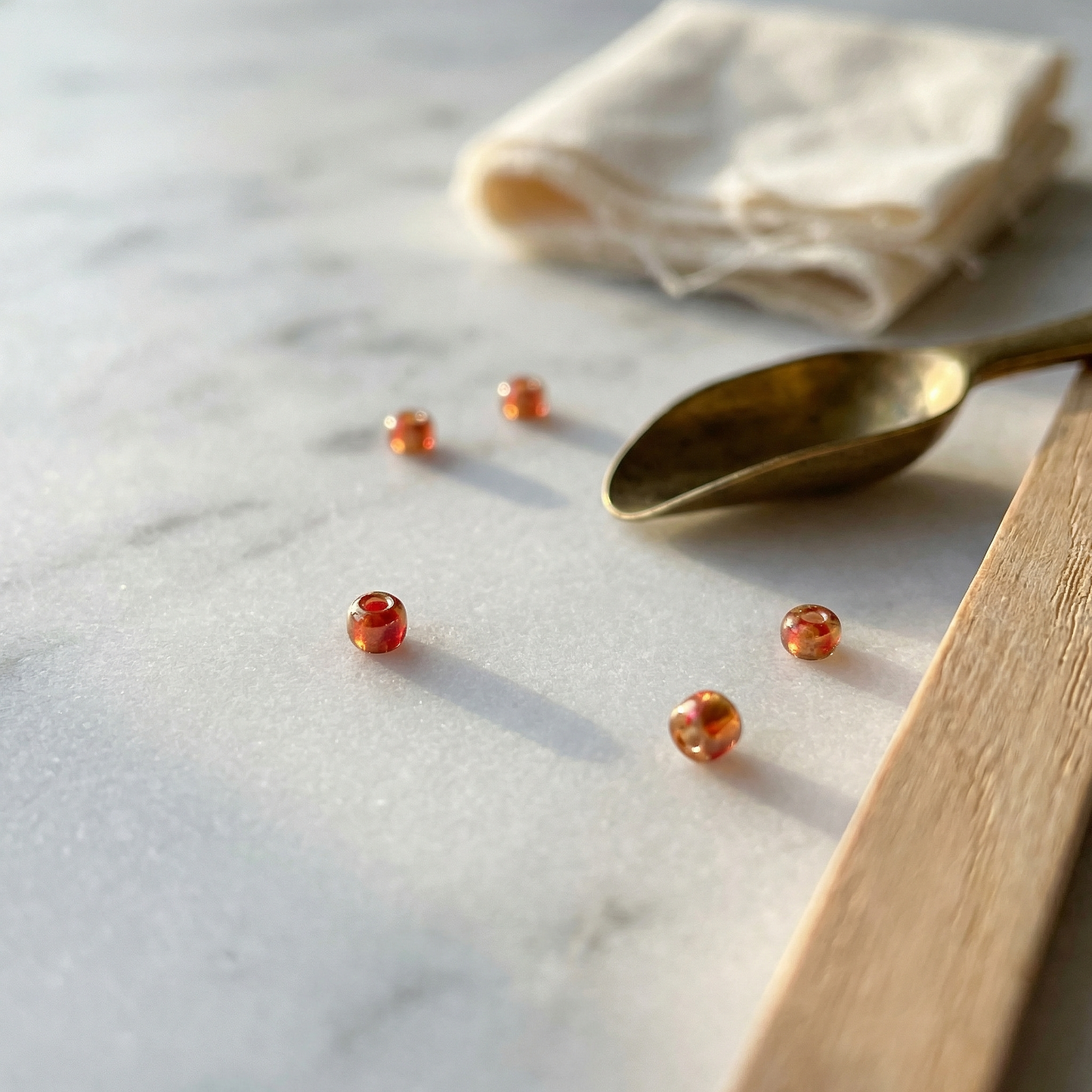 Cherry-gold seed bead on marble with soft window light, oak reflector, muslin and scoop