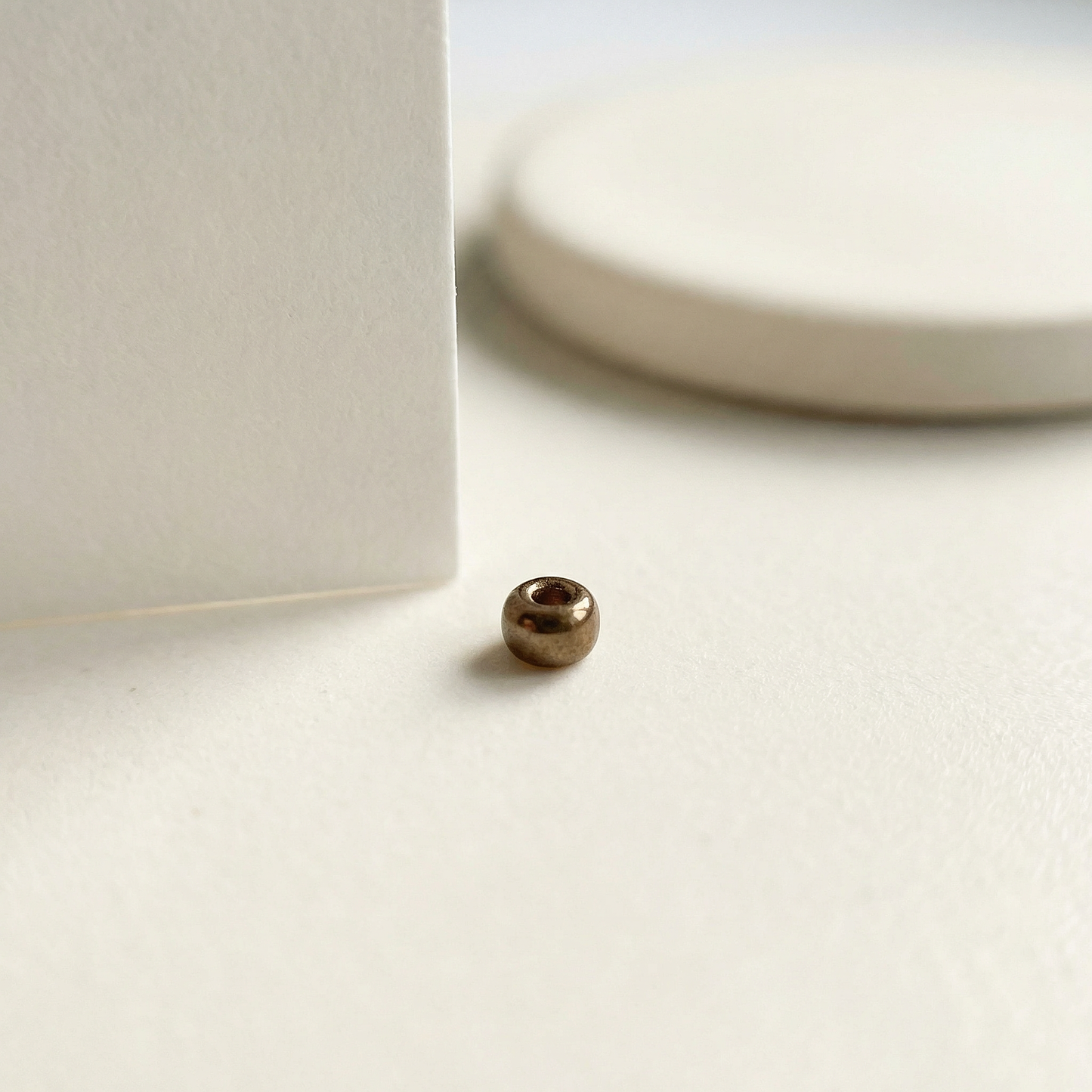 Single metallic brown Miyuki 15/0 bead on eggshell tile with folded paper edge