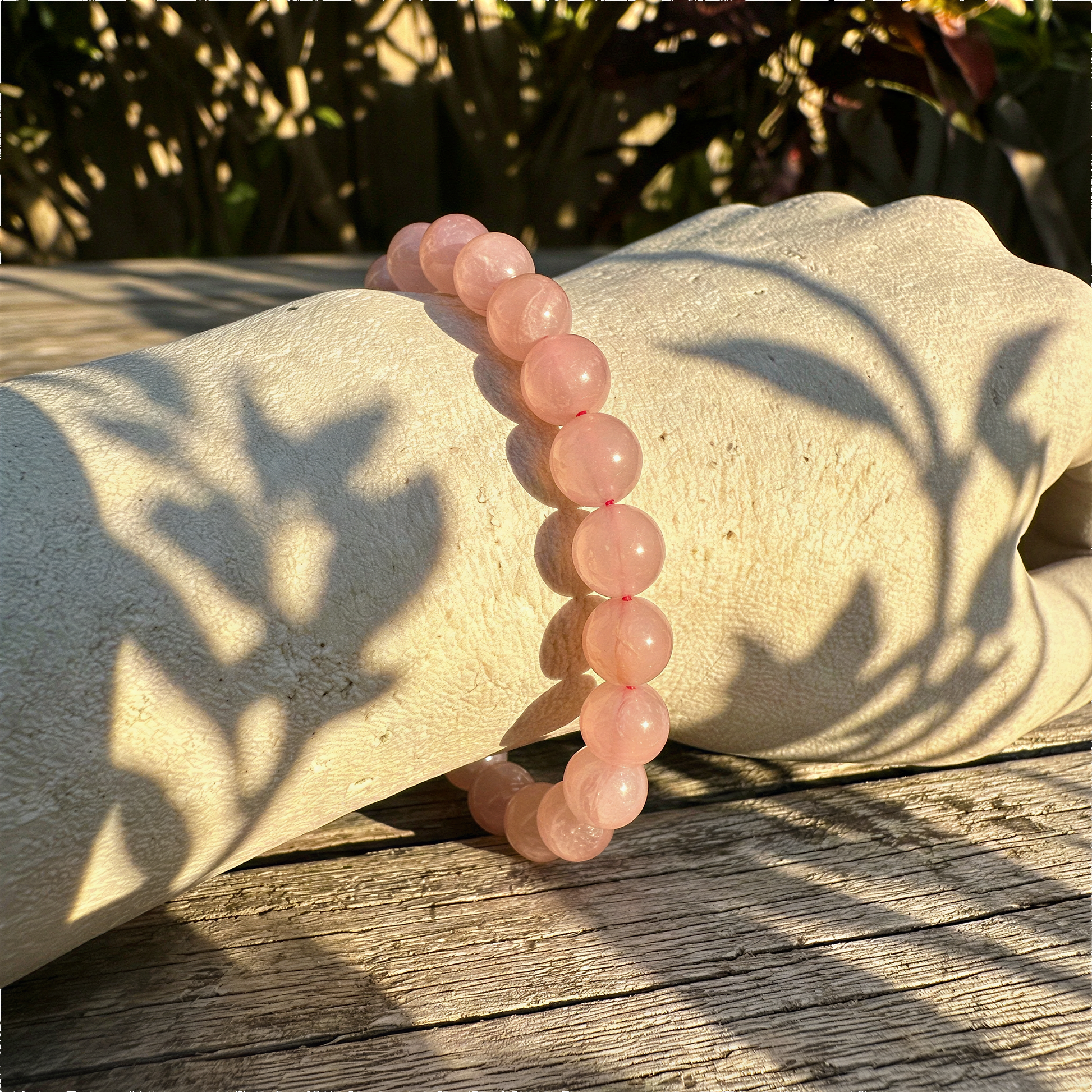 Madagascar rose quartz stretchy cord bracelet worn on wrist outdoors in warm daylight, serene natural setting