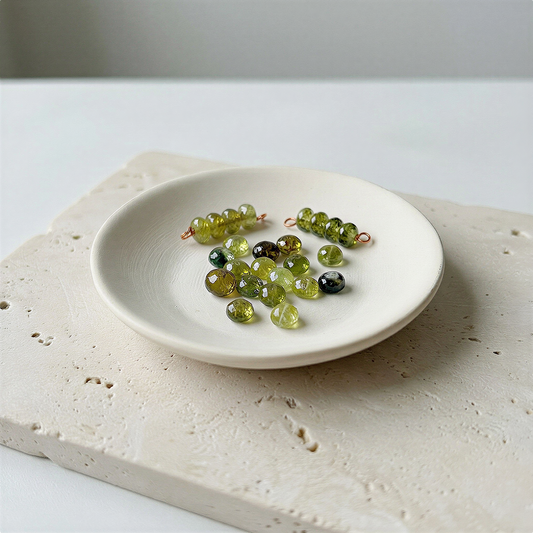 Faceted green garnet rondelle bead resting on soft neutral silk with balanced, calm lighting.