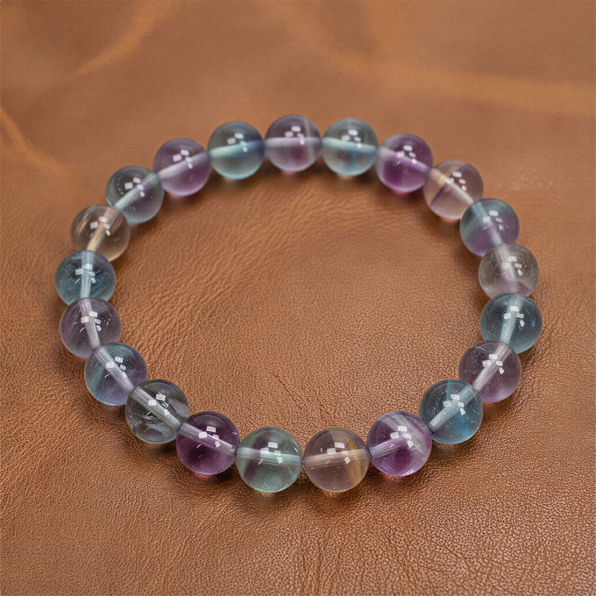Rainbow fluorite stretchy bracelet with varied bead sizes resting on jade stone in soft, diffused light.