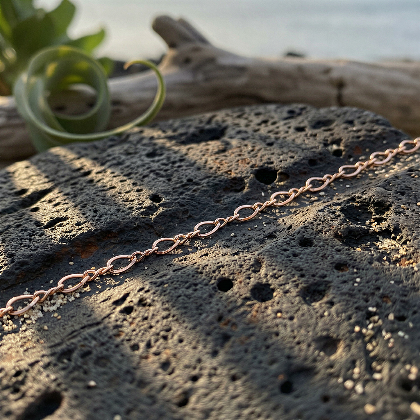 Rose gold filled figure eight chain draped on sunlit stone with tropical greenery and warm island tones