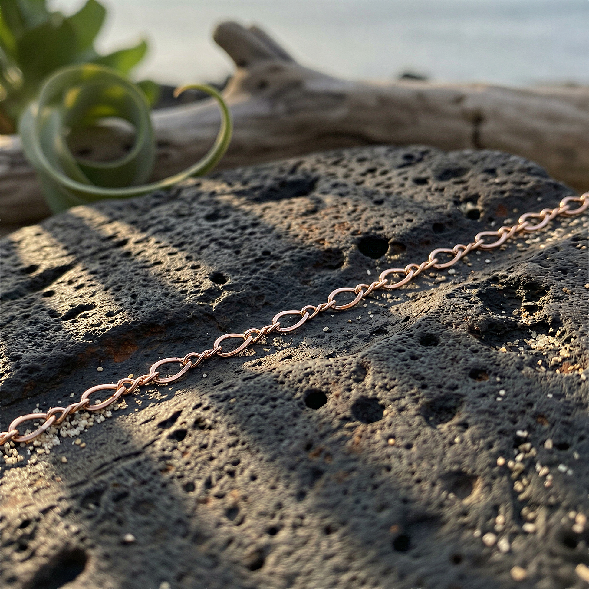 Rose gold filled figure eight chain draped on sunlit stone with tropical greenery and warm island tones