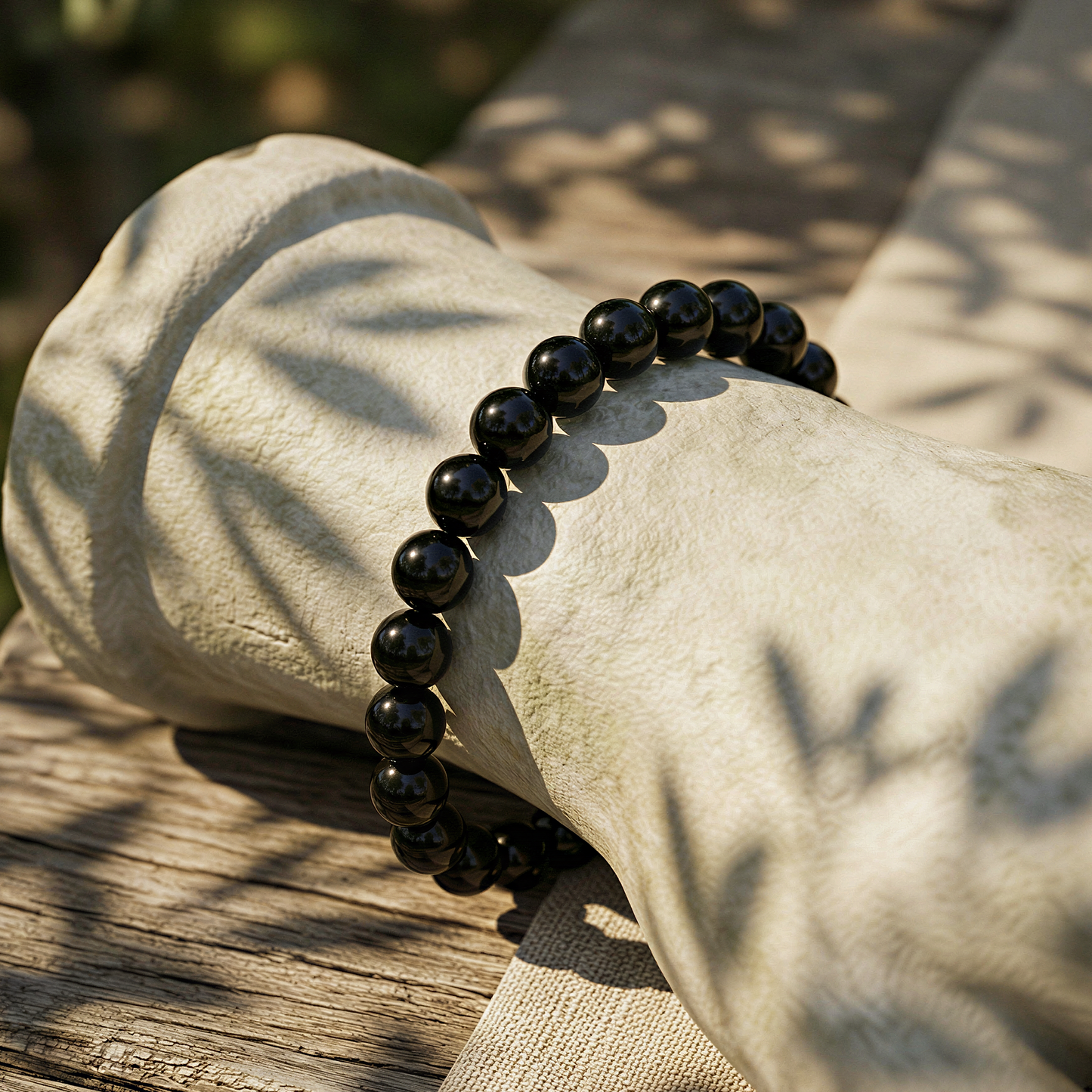 Black tourmaline 6mm smooth round bracelet worn outdoors, warm golden daylight, relaxed wrist among natural greenery.
