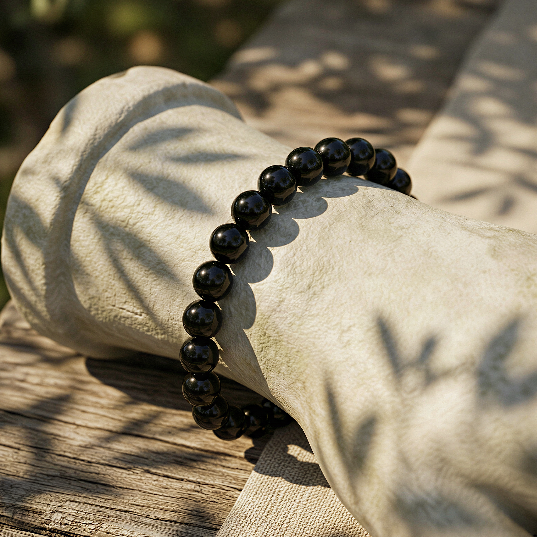 Black tourmaline 6mm smooth round bracelet worn outdoors, warm golden daylight, relaxed wrist among natural greenery.