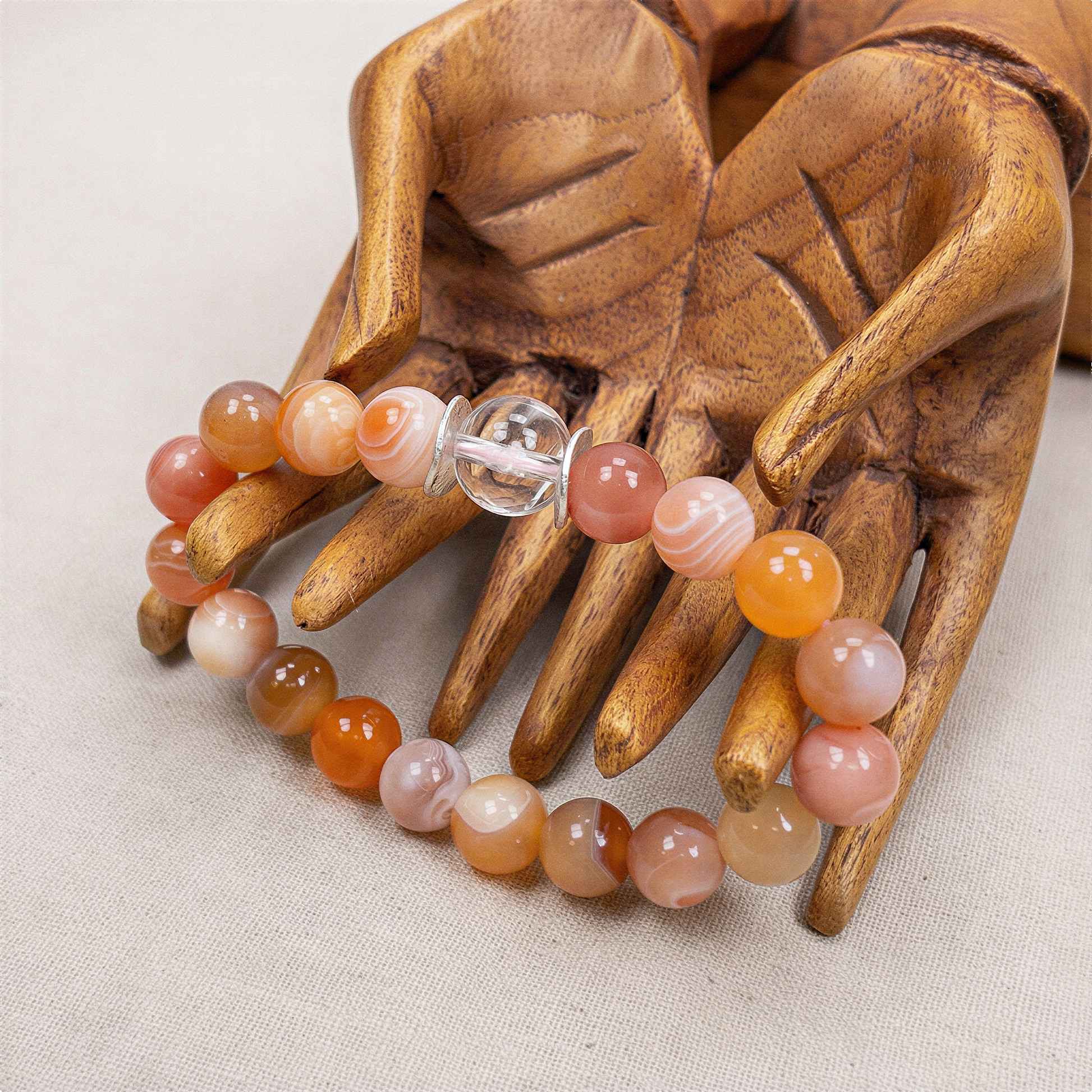 Cherry blossom stretchy bracelet kit displayed on a wooden hand, featuring agate beads and a clear quartz focal bead with delicate pink sakura blooms glowing inside soft studio light.