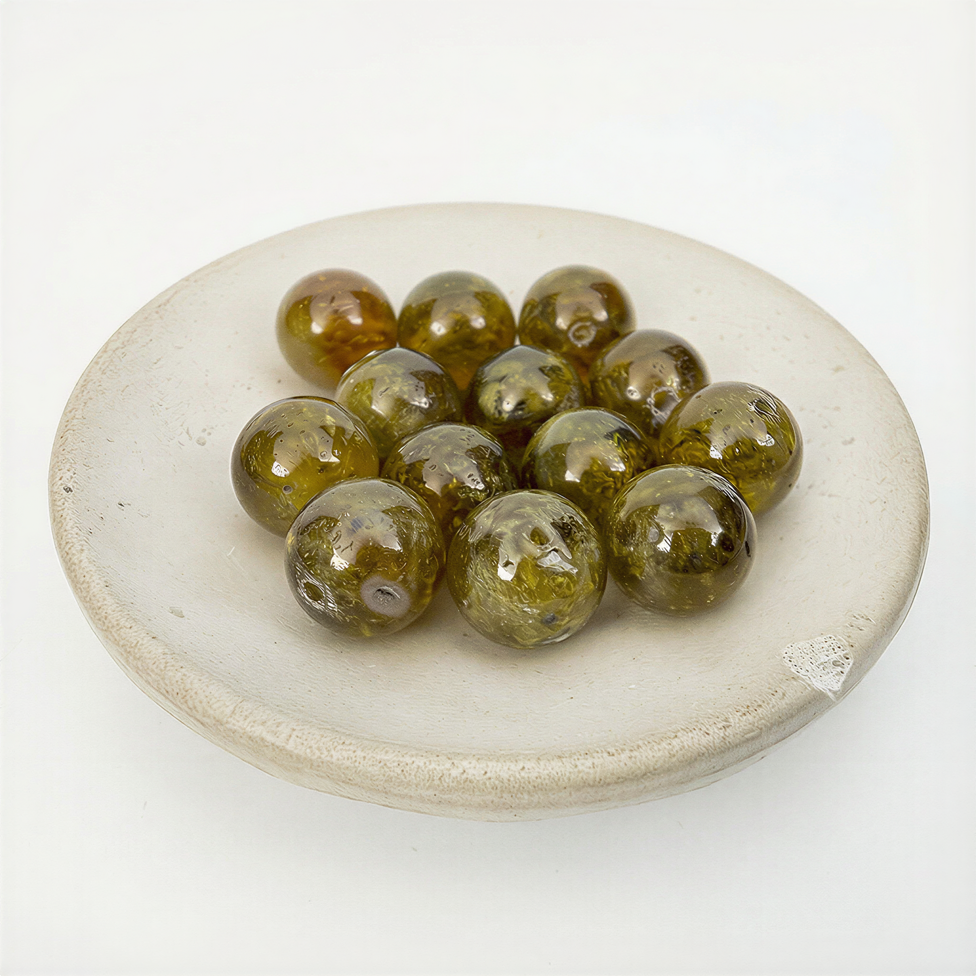 Eleven olive‑green garnet beads glowing with soft translucence, arranged in a matte ceramic dish against an airy off‑white backdrop.