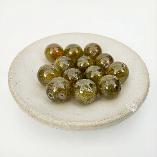 Eleven olive‑green garnet beads glowing with soft translucence, arranged in a matte ceramic dish against an airy off‑white backdrop.