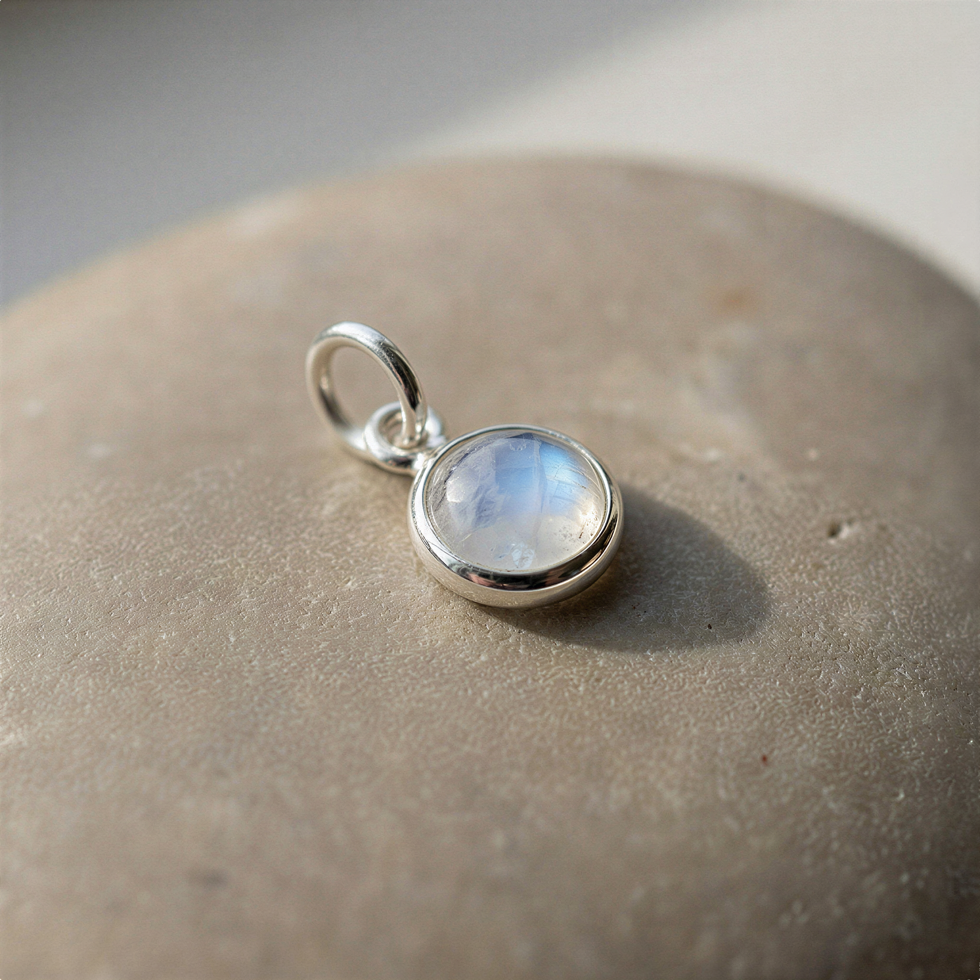 Rainbow moonstone bezel pendant in sterling silver on neutral backdrop with soft diffused light enhancing clarity