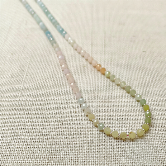 Soft mixed beryl beads in gentle pastel hues drape as a continuous strand on textured linen, lit with airy natural light.