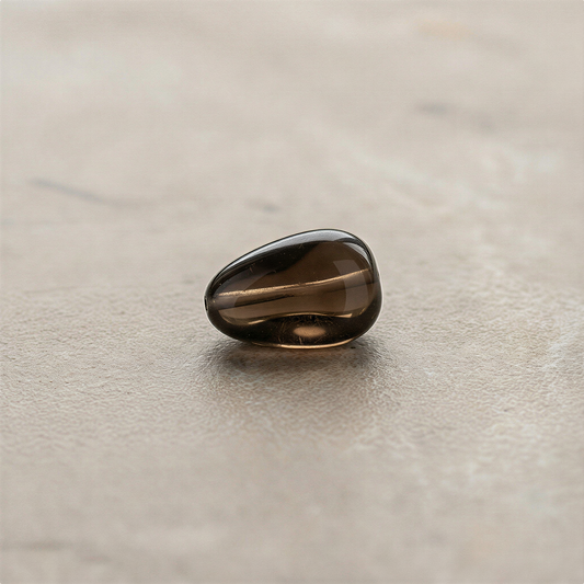 Smoky quartz tumbled nugget bead displayed on neutral surface with soft studio lighting enhancing natural depth