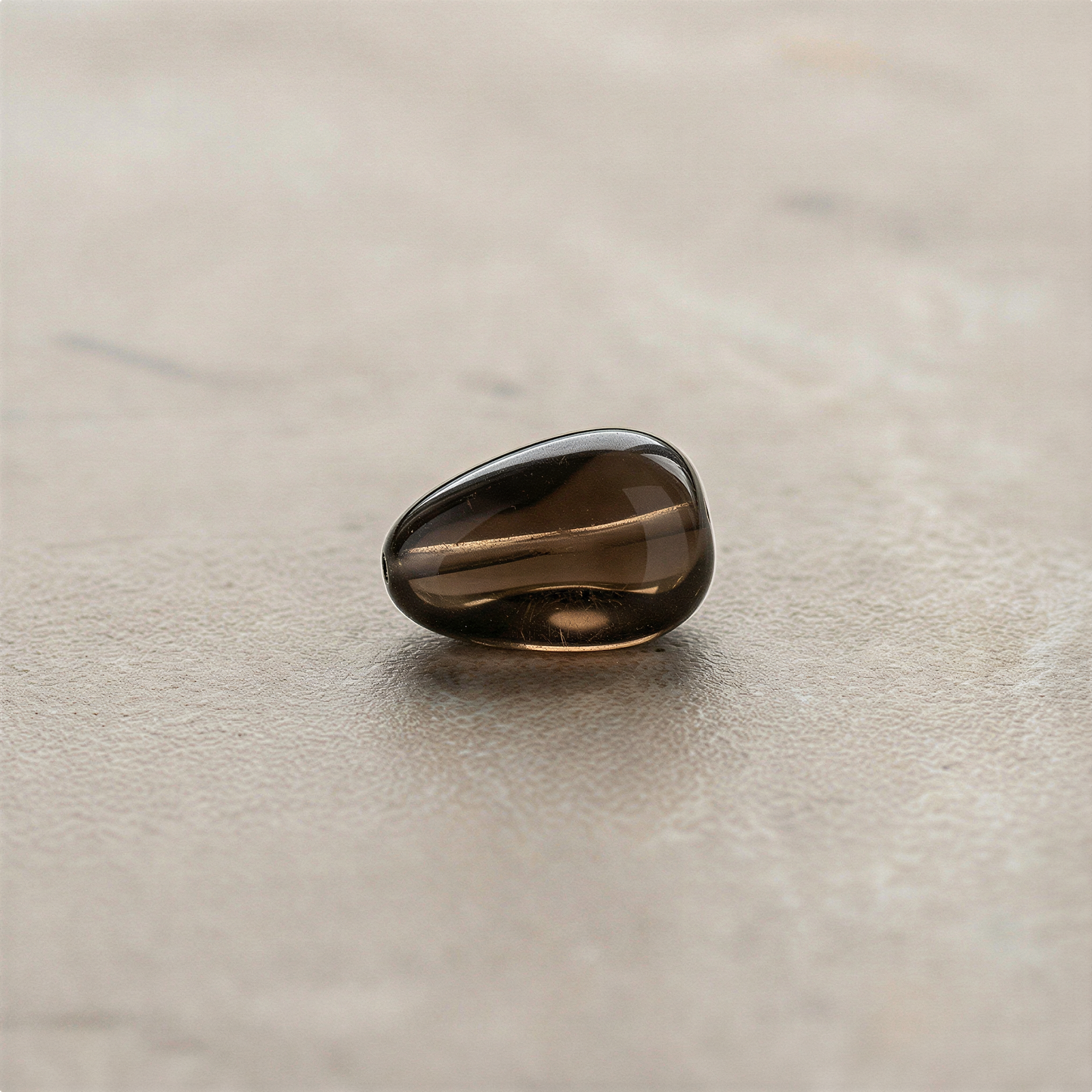 Smoky quartz tumbled nugget bead displayed on neutral surface with soft studio lighting enhancing natural depth