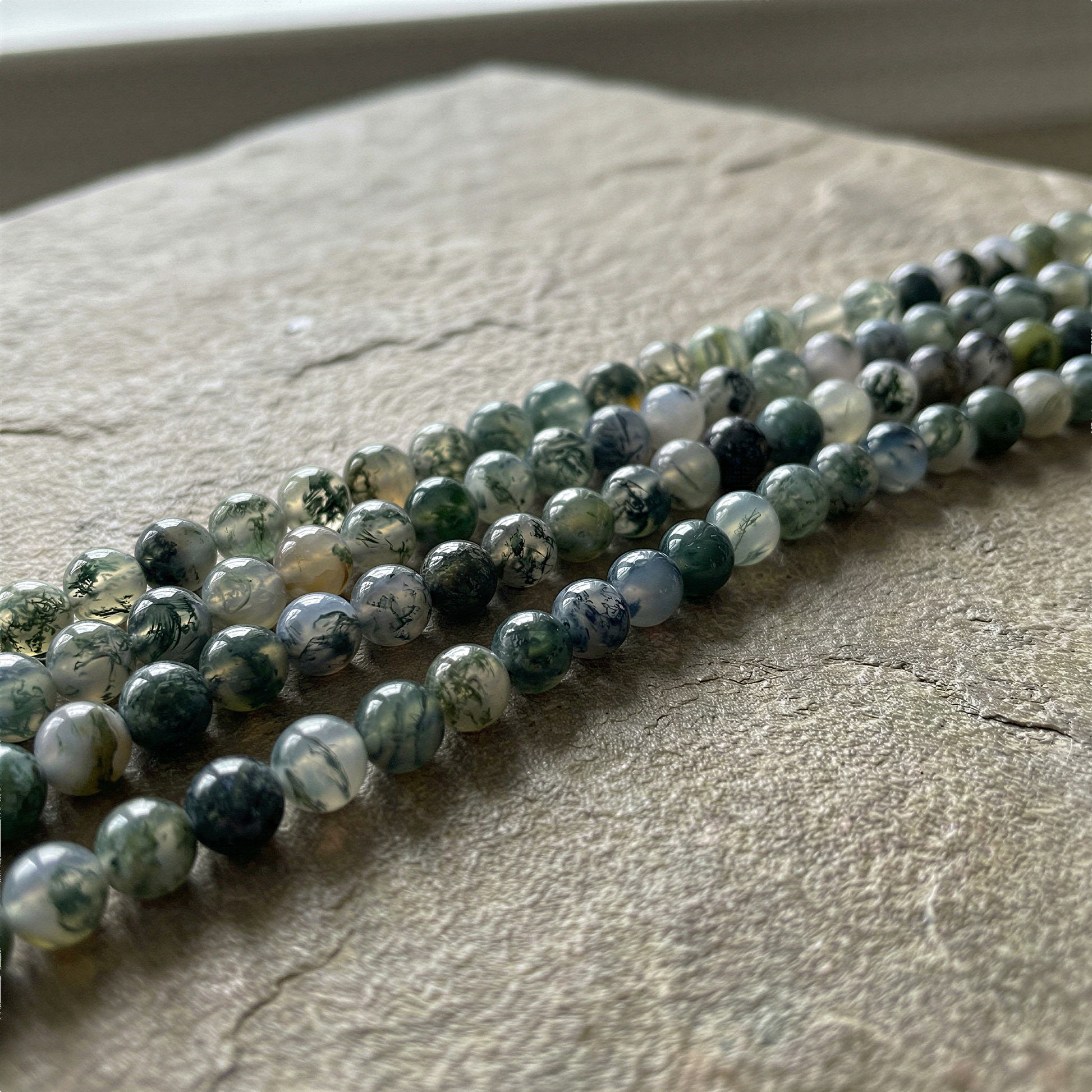 Moss agate 6mm round bead strand laid naturally, enhanced clarity revealing soft green inclusions and organic texture
