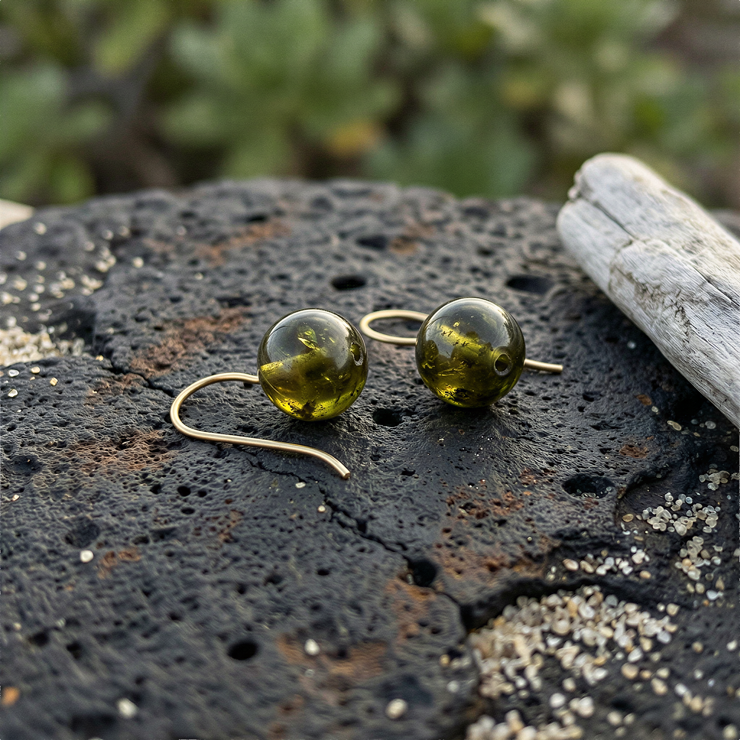 Single 10mm green garnet bead resting on volcanic sand with tropical leaves in soft natural light