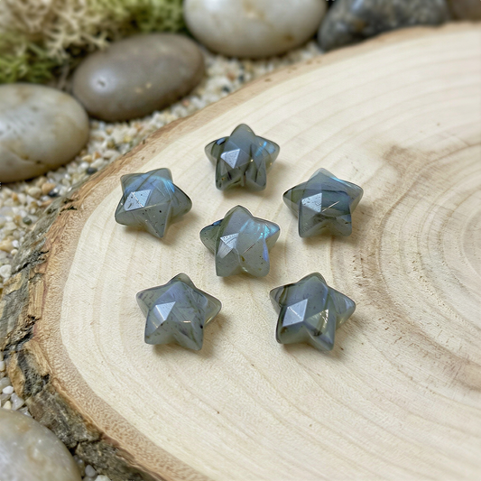 Faceted labradorite star briolette bead resting on a soft natural wood background, glowing with blue flashes under gentle, diffused daylight.