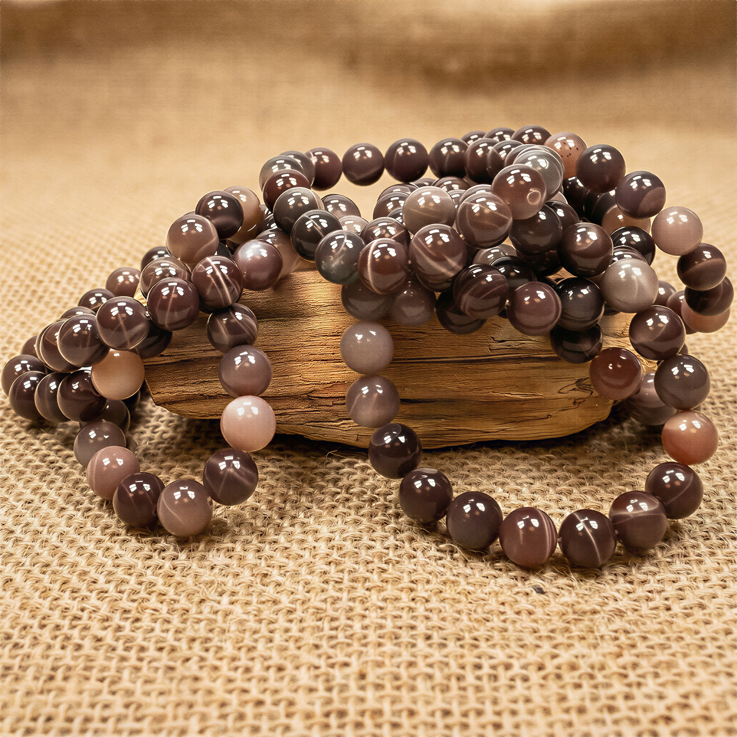 Chocolate moonstone bead bracelet with polished 10mm round gems, resting on softly blurred burlap fabric under warm, even light