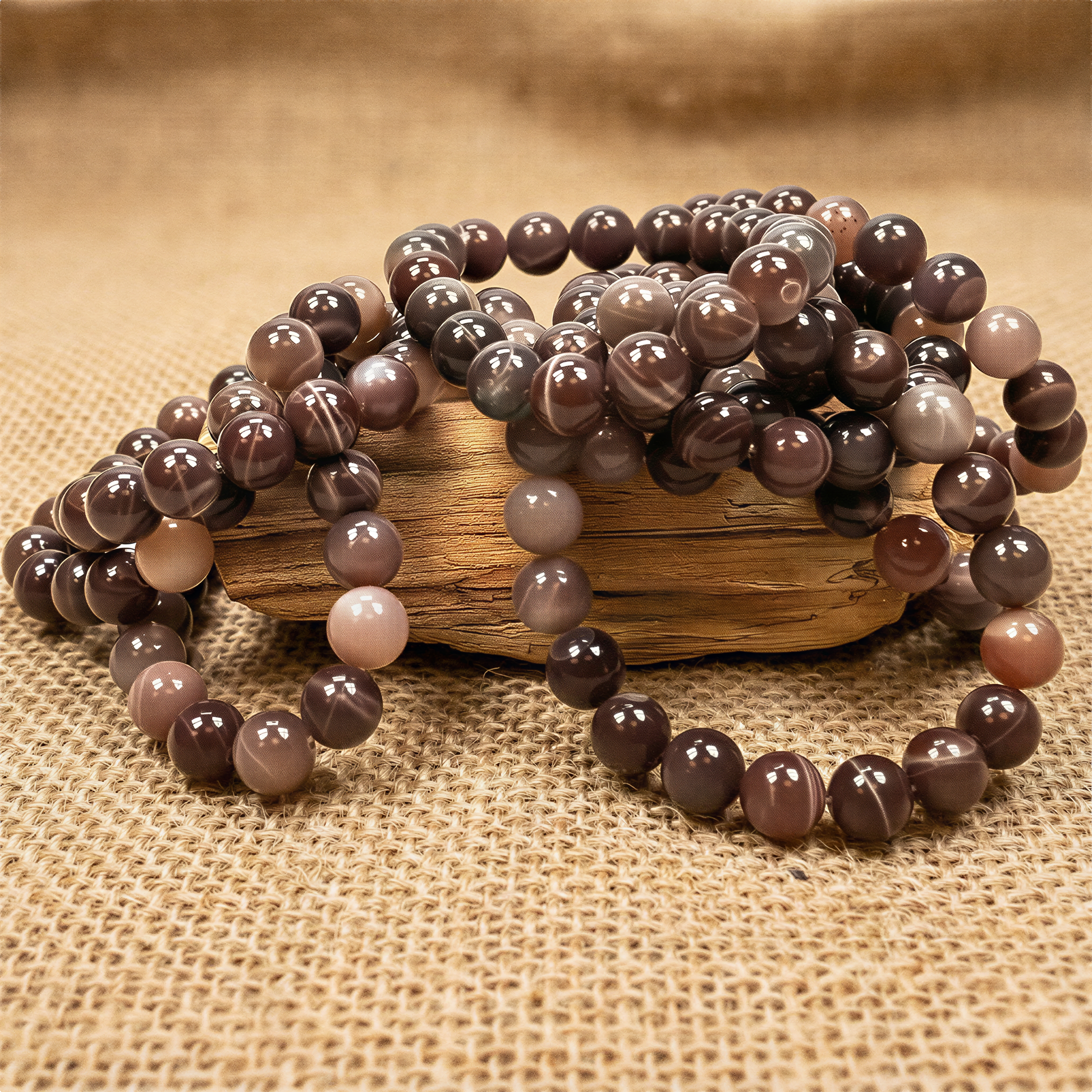 Chocolate moonstone bead bracelet with polished 10mm round gems, resting on softly blurred burlap fabric under warm, even light