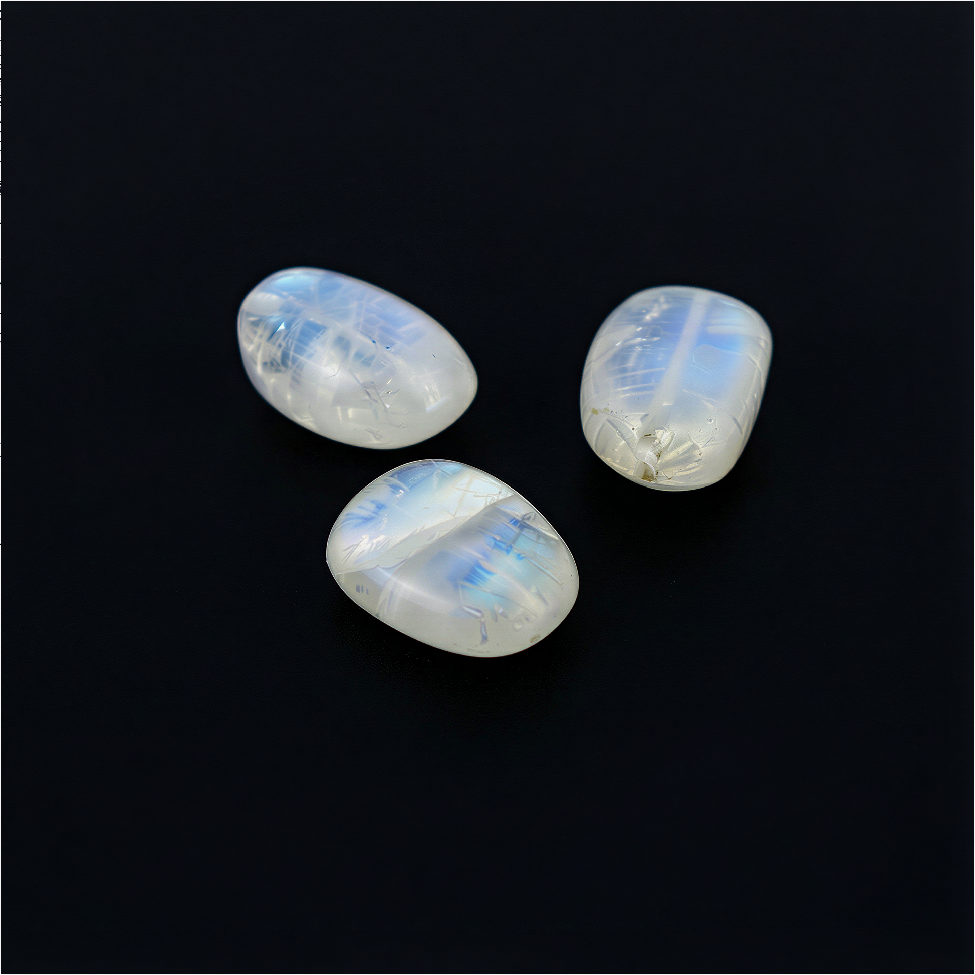 Single rainbow moonstone nugget bead floating against a deep black background, glowing with soft blue flashes and natural translucent texture
