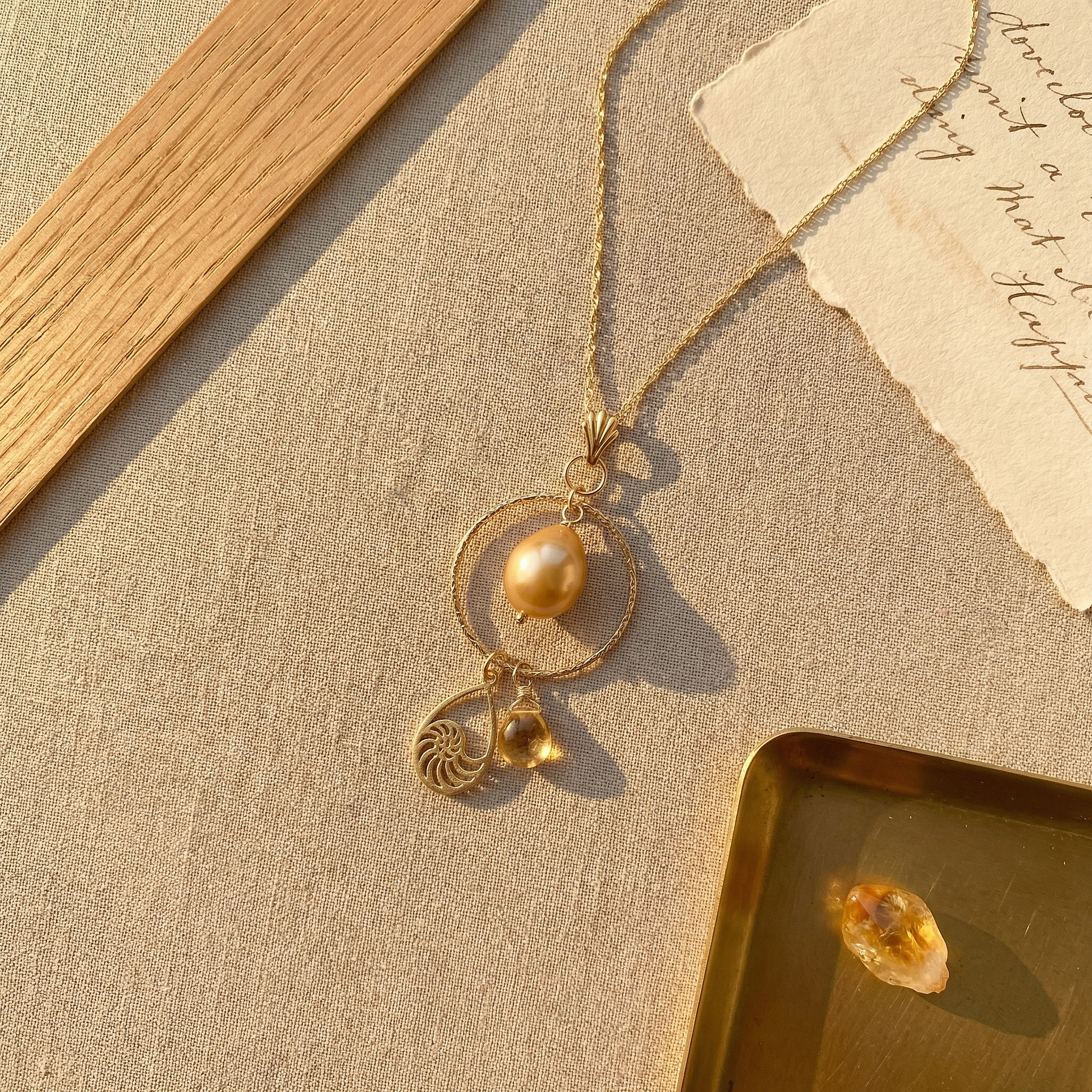 Overhead flat-lay of hammered vermeil hoop necklace with golden pearl and citrine on warm linen.