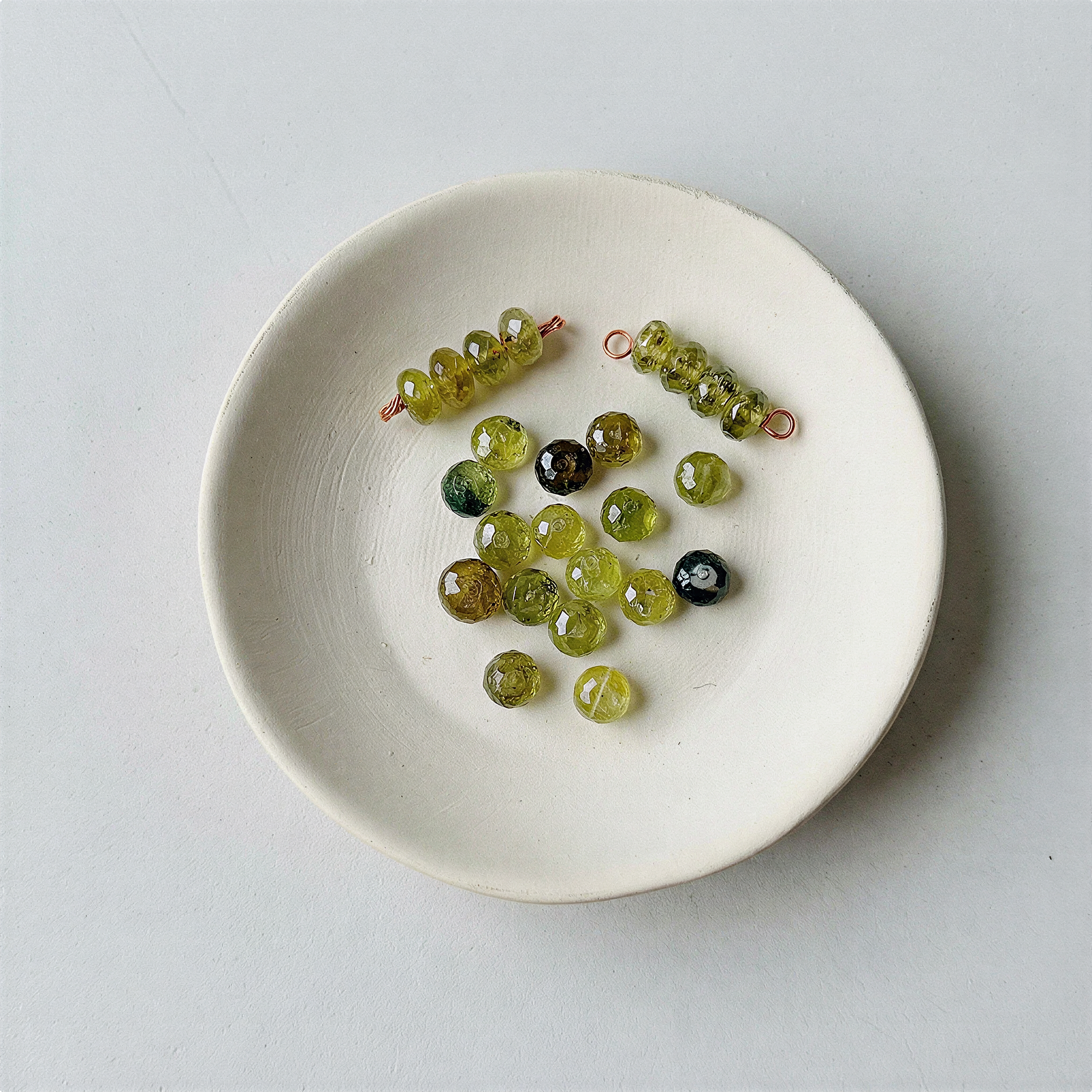 Faceted green garnet rondelle bead resting on natural stone surface in soft, diffused daylight