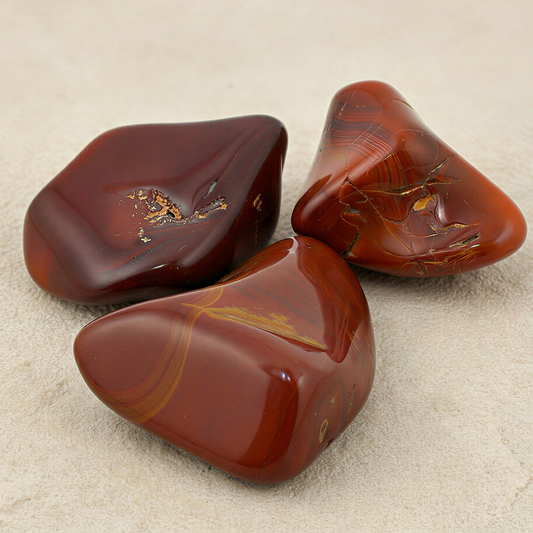 Dark red carnelian tumbled stone on neutral stone surface with refined lighting enhancing natural clarity and depth