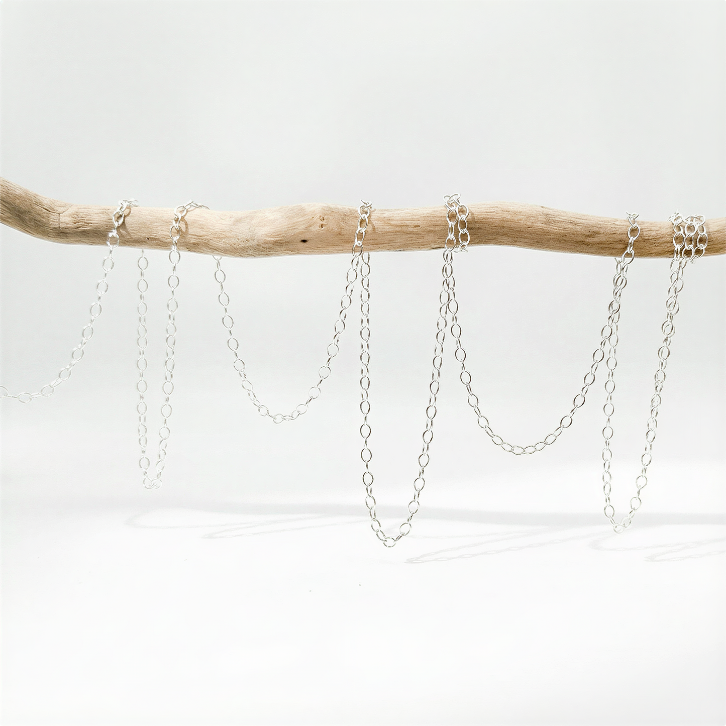 Small fluffy cable chain in silver and gold tones on neutral surface with refined, natural light