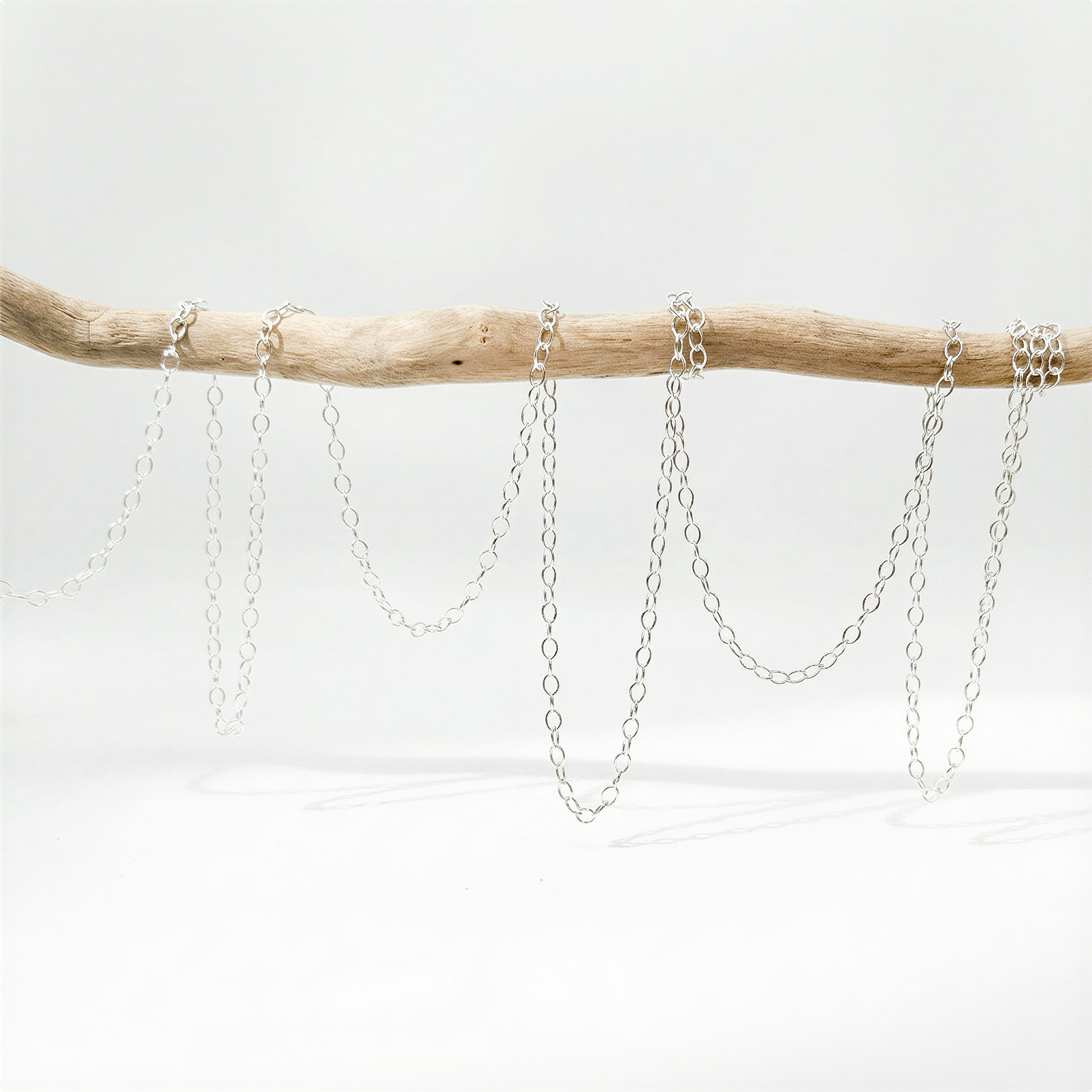 Small fluffy cable chain in silver and gold tones on neutral surface with refined, natural light