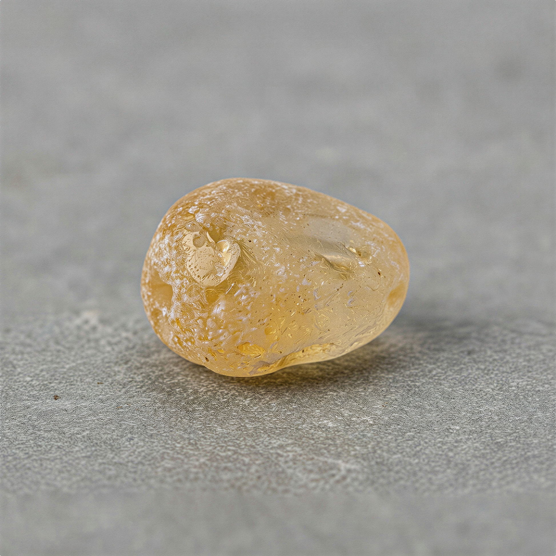 Frosted citrine rough tumbled nugget bead with long drill hole on neutral studio surface, softly enhanced clarity.