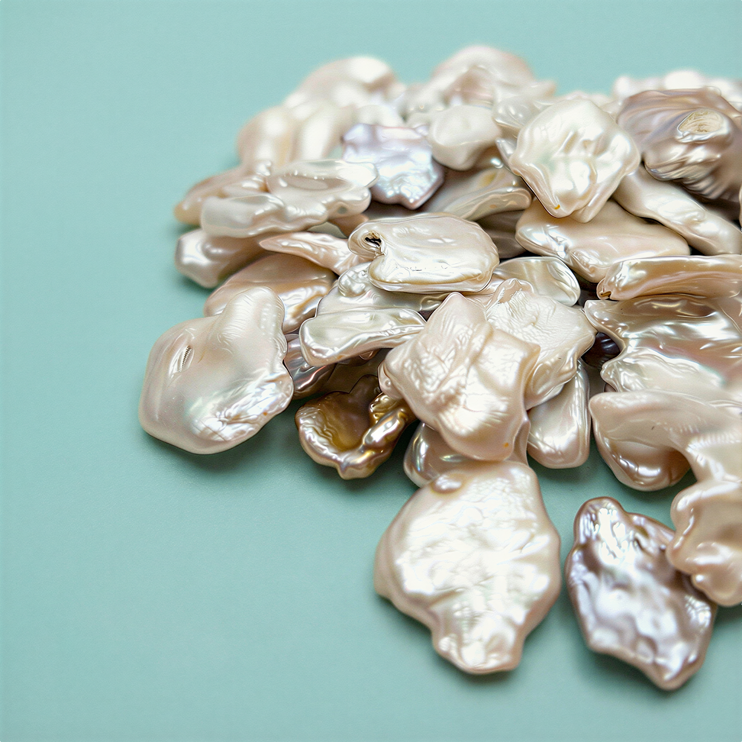 Four oversized baroque pearl beads glowing with natural iridescence, softly lit against a clean aqua backdrop that enhances their organic shapes and luminous texture.