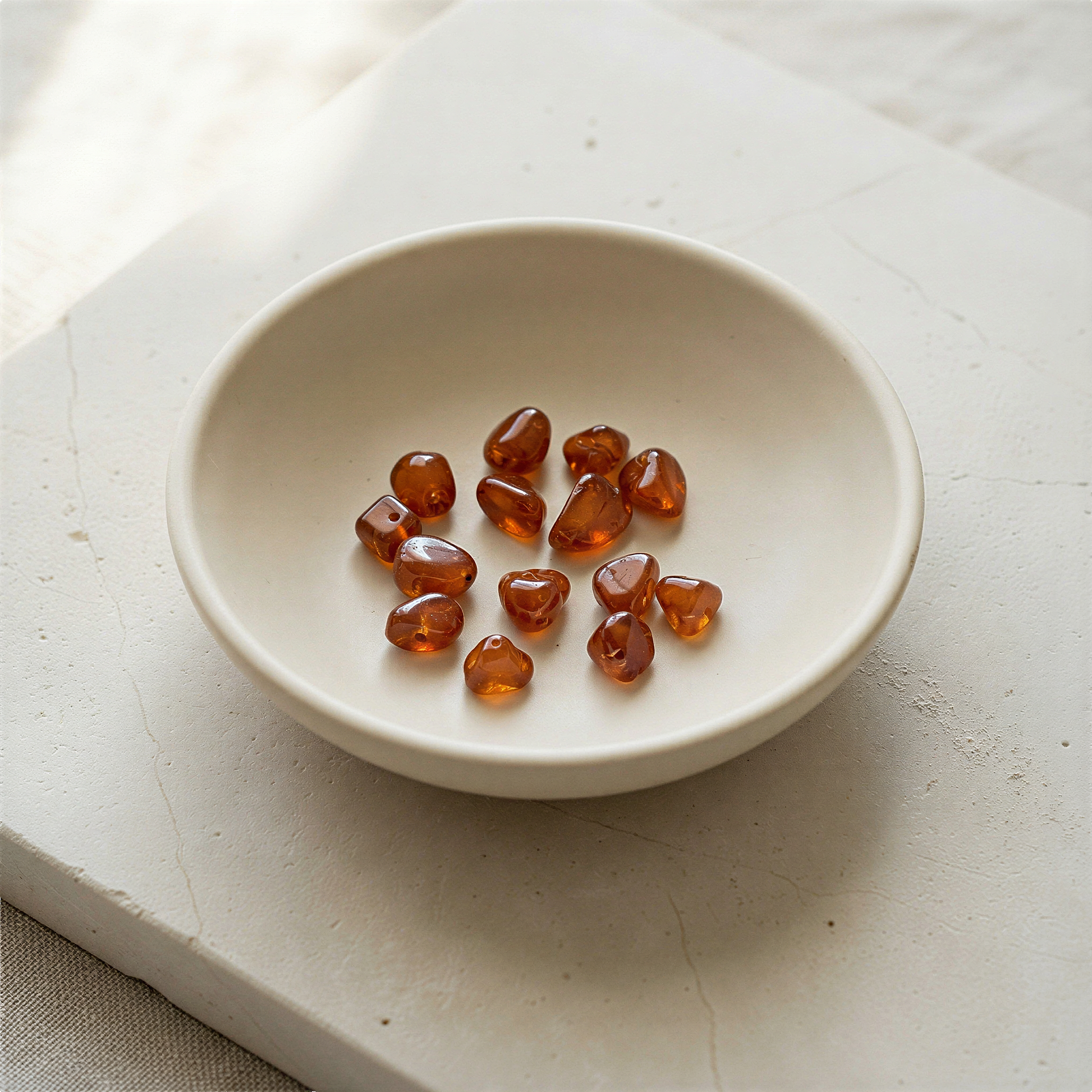 Tiny spessartite garnet tumbled nugget bead resting on natural stone surface in soft, ambient daylight