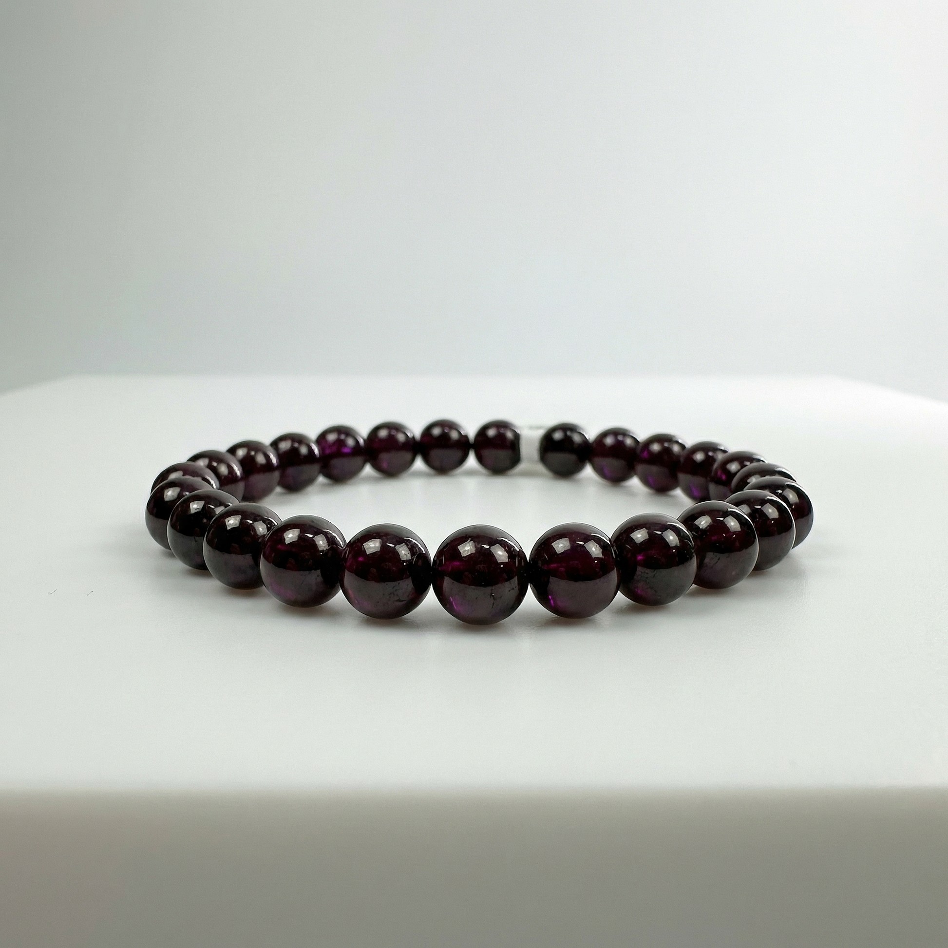 Rhodolite garnet bead bracelet on white acrylic with soft overhead light and violet inner glow.