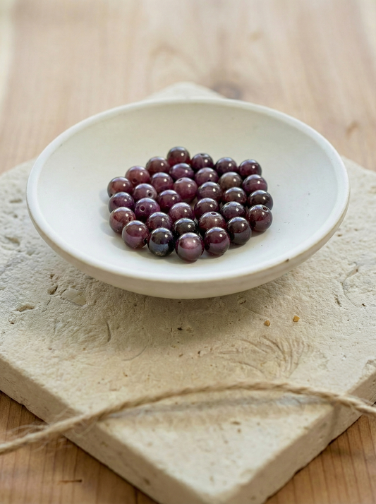 Row of polished 6mm star garnet beads with soft daylight sheen; front bead shows a muted six‑ray asterism and shallow depth of field.