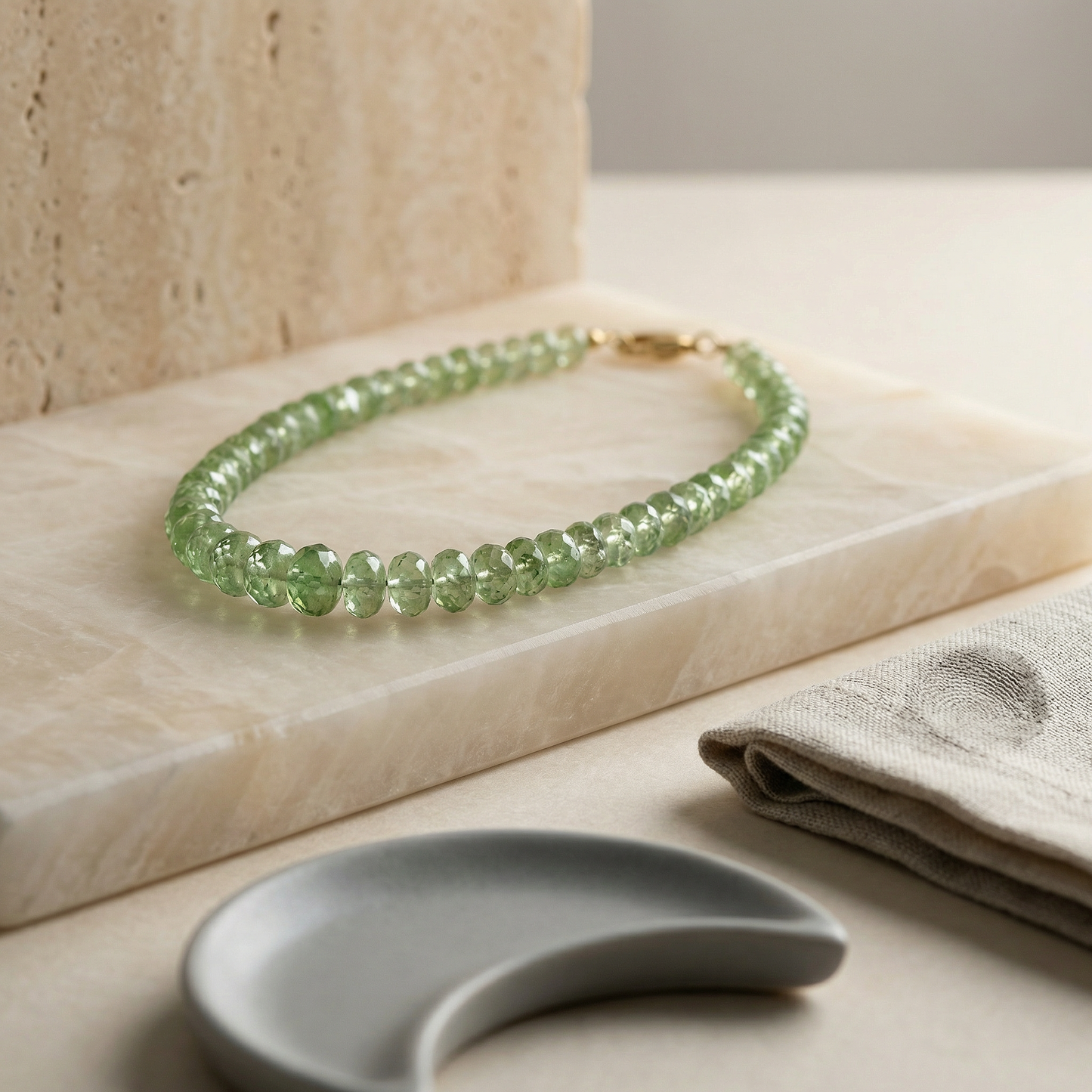 Graduated tsavorite rondelle beads on alabaster with linen, travertine, and soft gray ceramic.