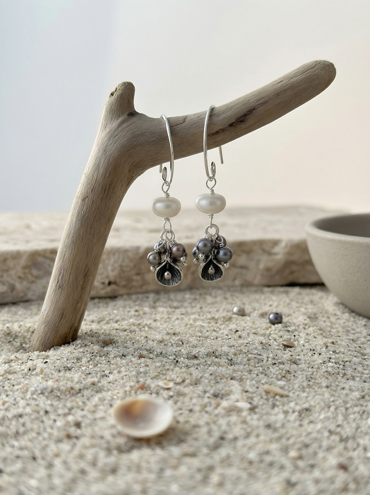 Sterling calla earrings hanging from driftwood over pale mineral sand with shells