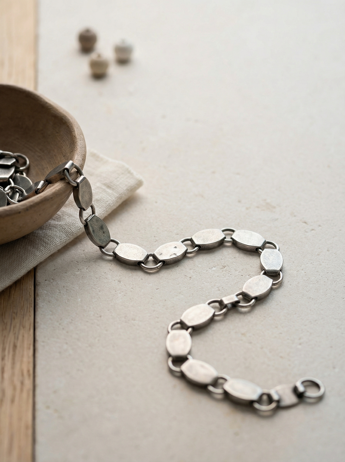 Antique silver trinket chain on honed limestone with clay bowl and oak strip.