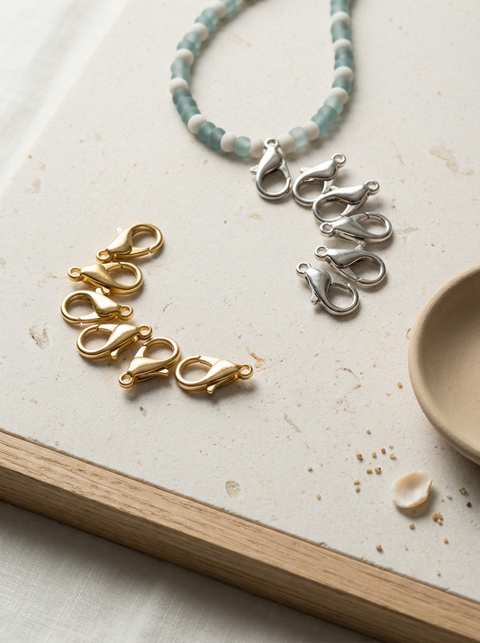 Gold and silver lobster clasps on honed limestone with oak strip and sea‑glass bead strand.