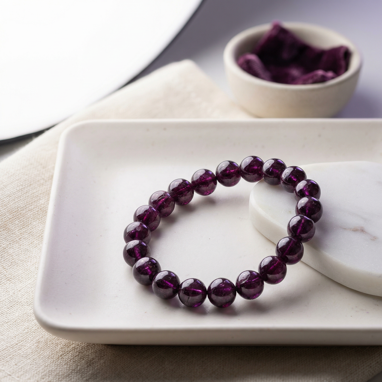 Rhodolite purple garnet bracelet on porcelain tray with marble and plum textile accents.