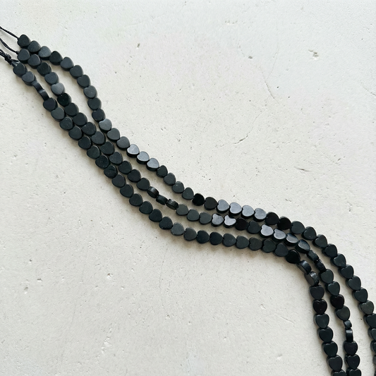 Black tourmaline heart beads strung on linen with soft natural light, evoking calm discovery.