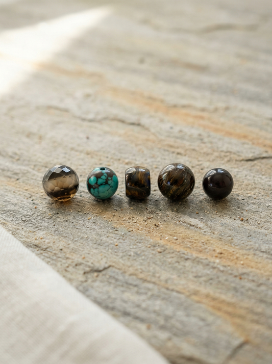 Five natural gemstone beads on weathered stone slab with soft morning light.