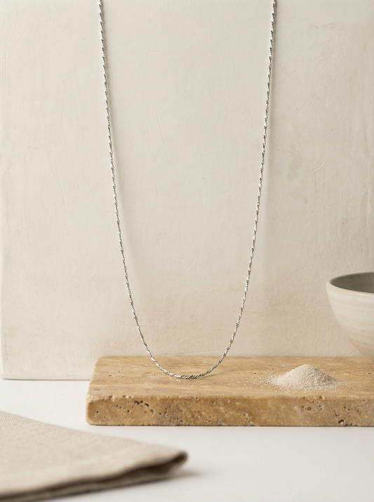Sterling serpentine chain on travertine and plaster backdrop with linen and pale sand