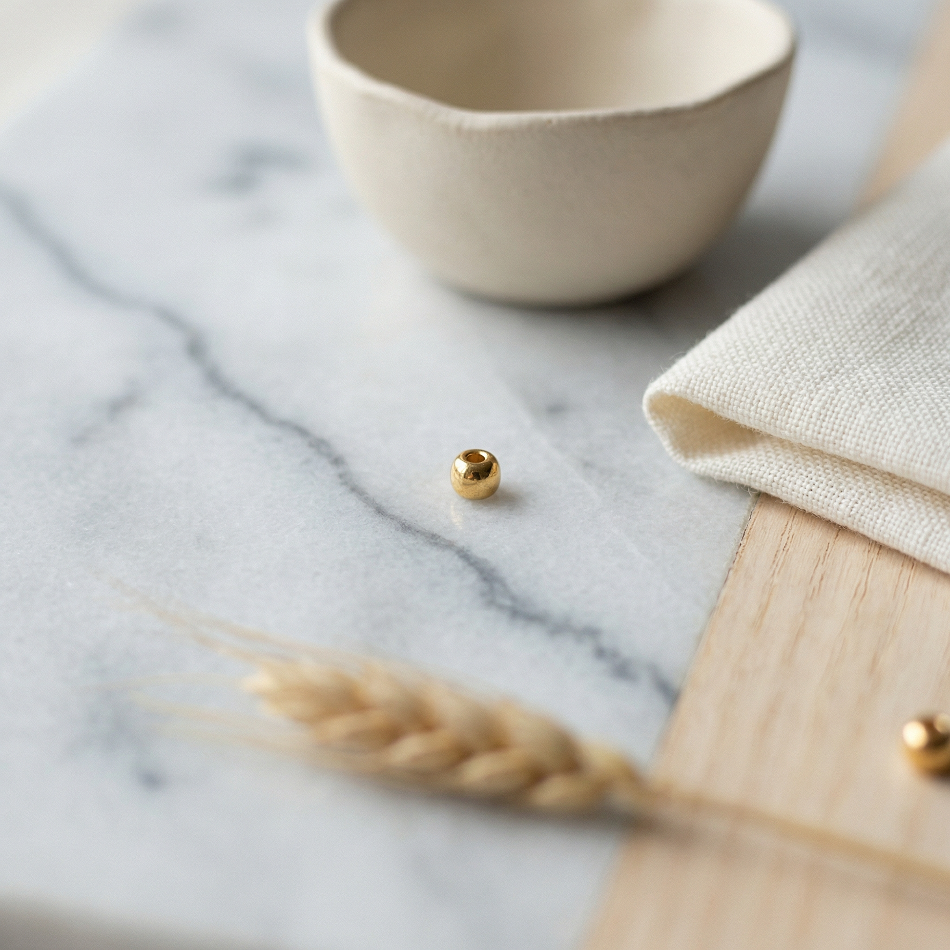 Gold seed bead on Carrara marble with linen, pale wood, and soft morning light