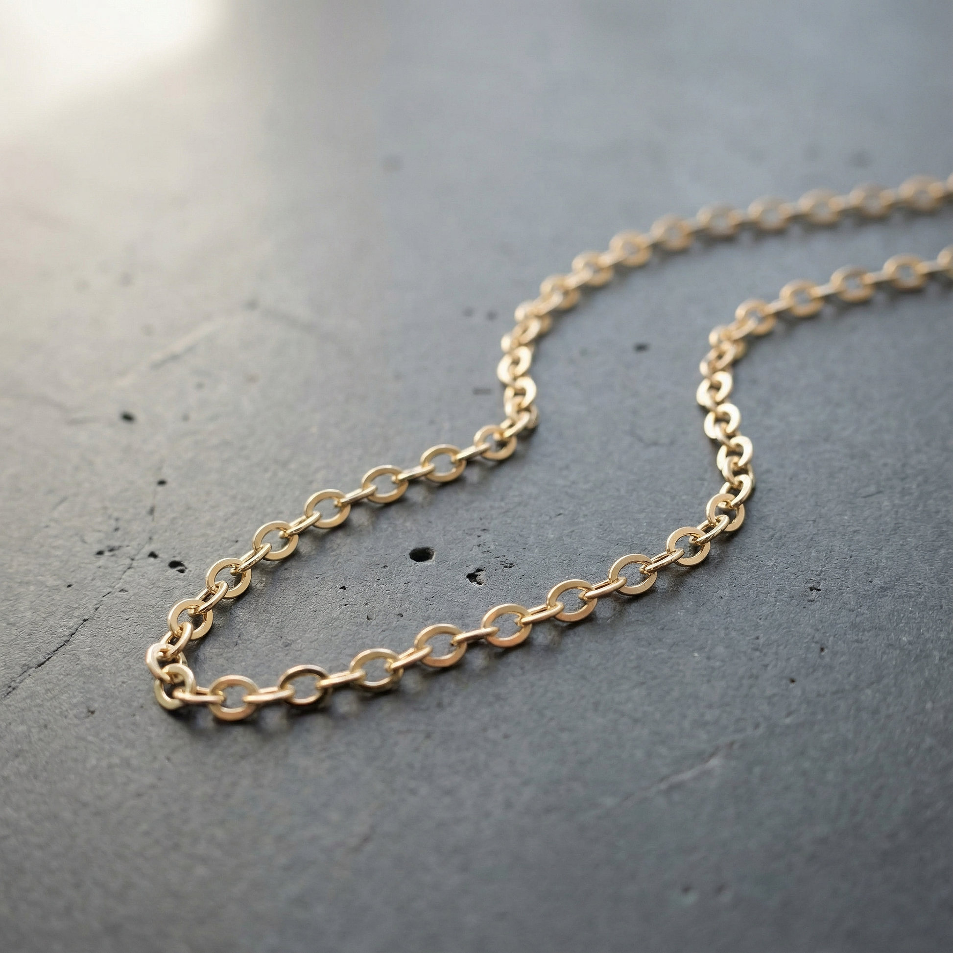 Delicate flat cable chain resting on sun-warmed stone, softly reflecting light amid a calm natural setting