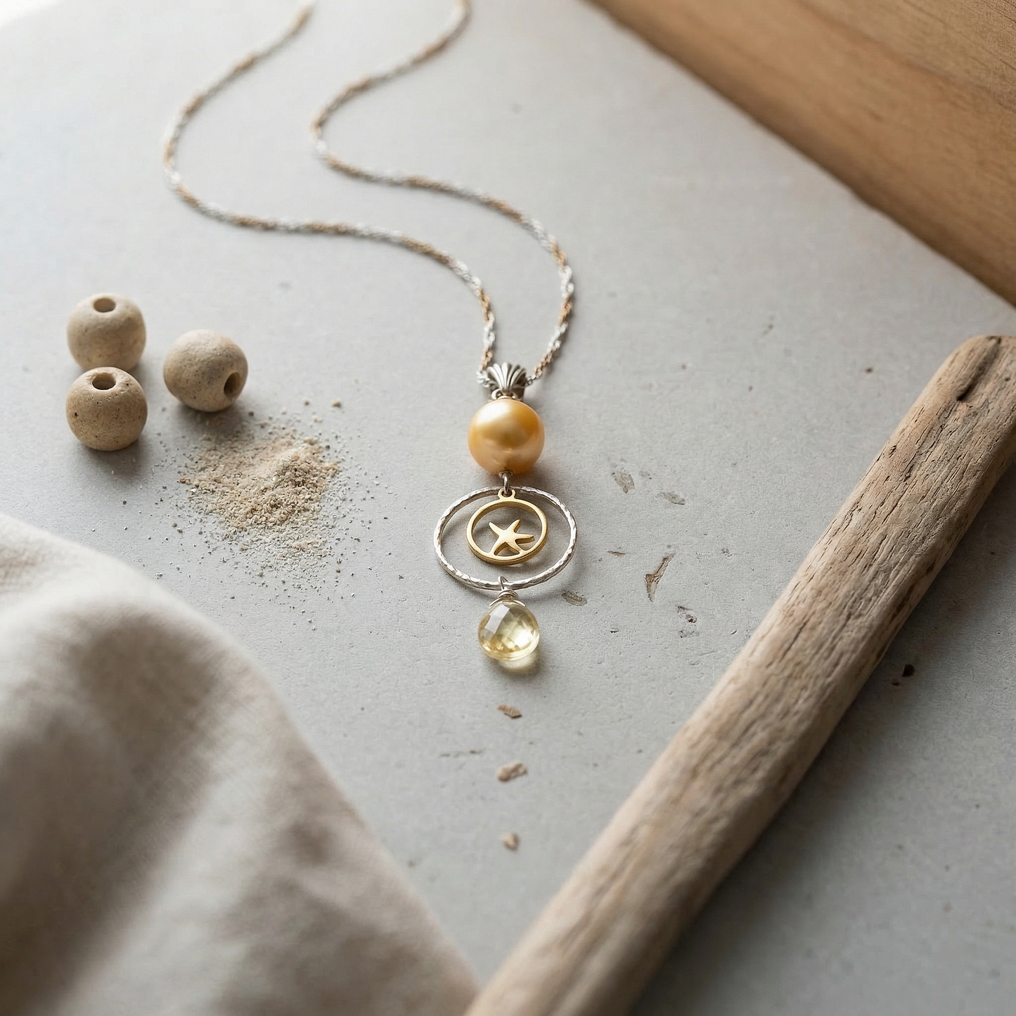 Golden pearl pendant on honed limestone with driftwood, ceramic beads, and soft linen light