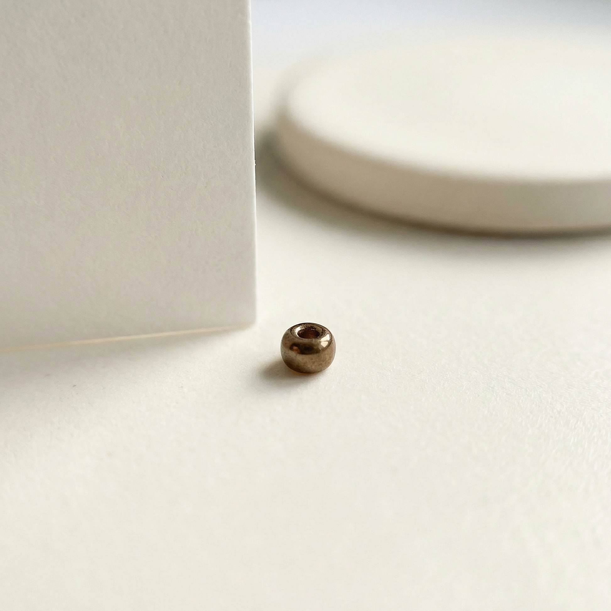 Single metallic brown Miyuki 15/0 bead on eggshell tile with folded paper edge