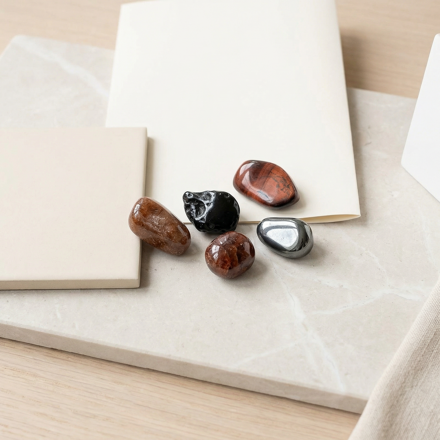 Tumbled garnet, tektite, spessartite, hematite and red tiger eye on pale surface